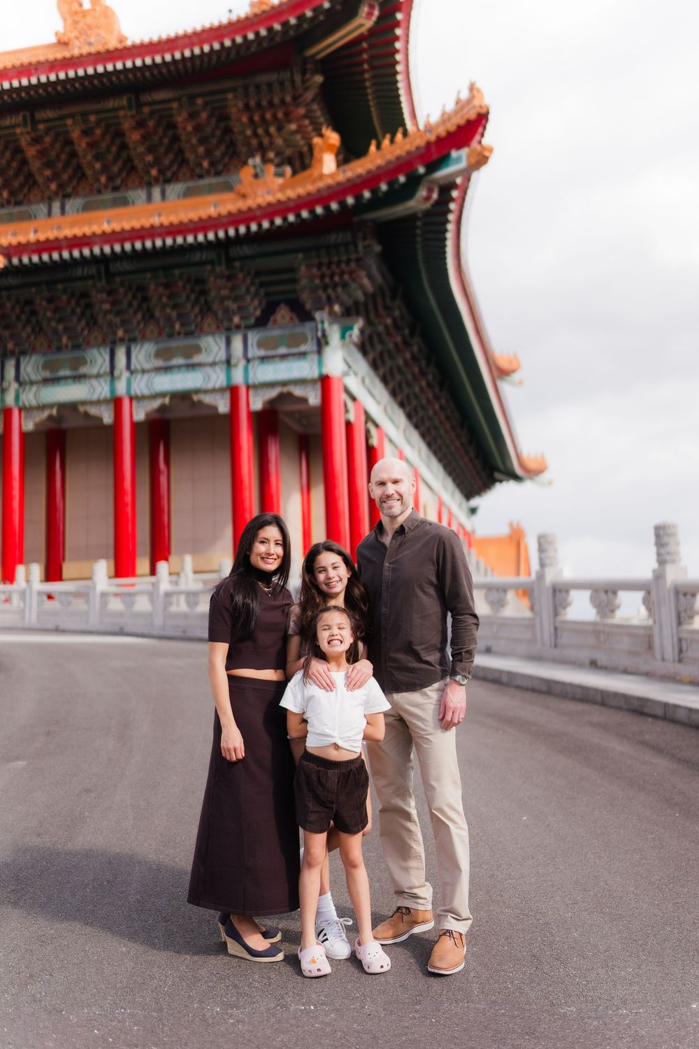 A family poses together outside a traditional Chinese temple with red pillars and ornate roofing in Taiwan.