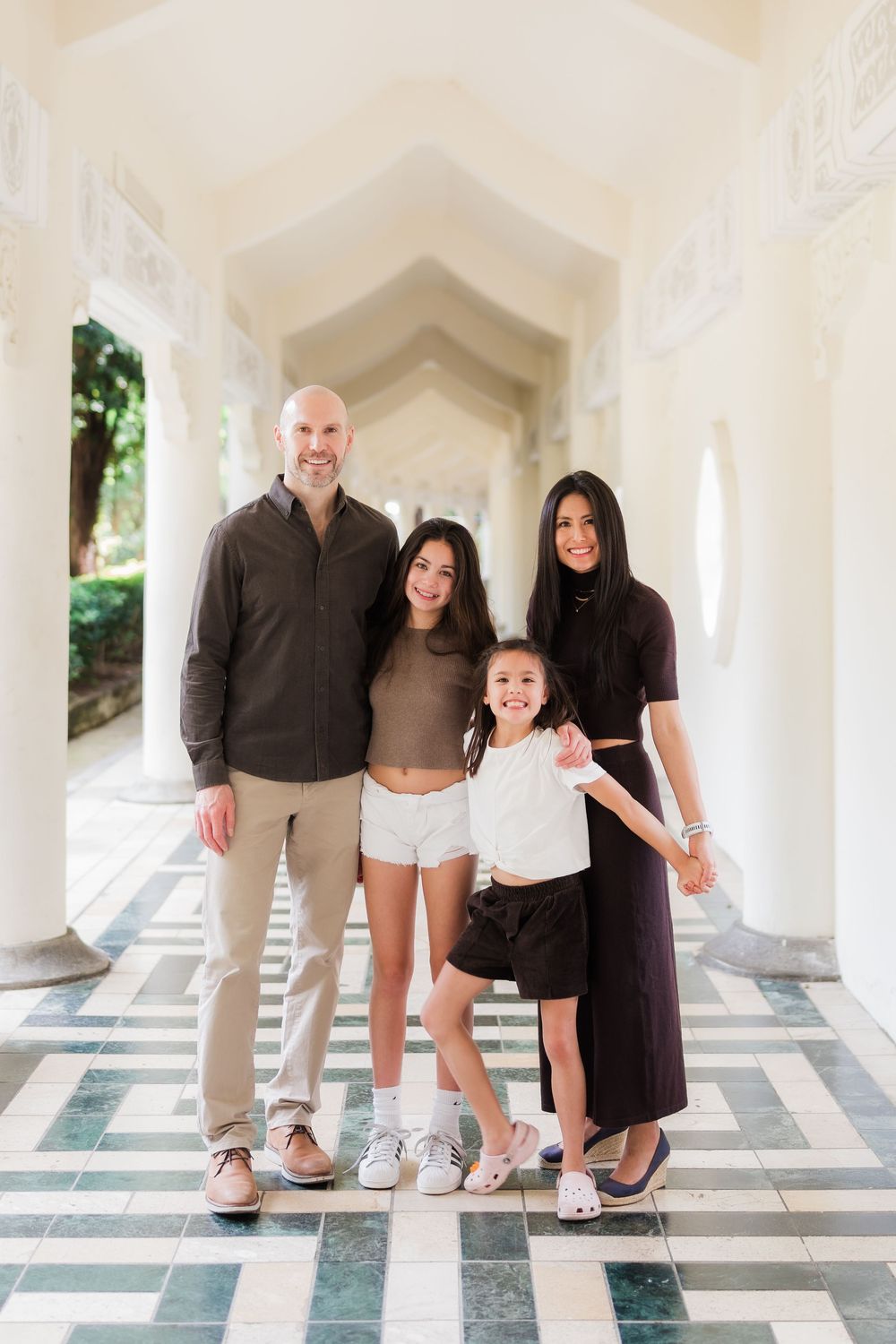 A family poses playfully in an outdoor colonnade with white columns and tiled floors.