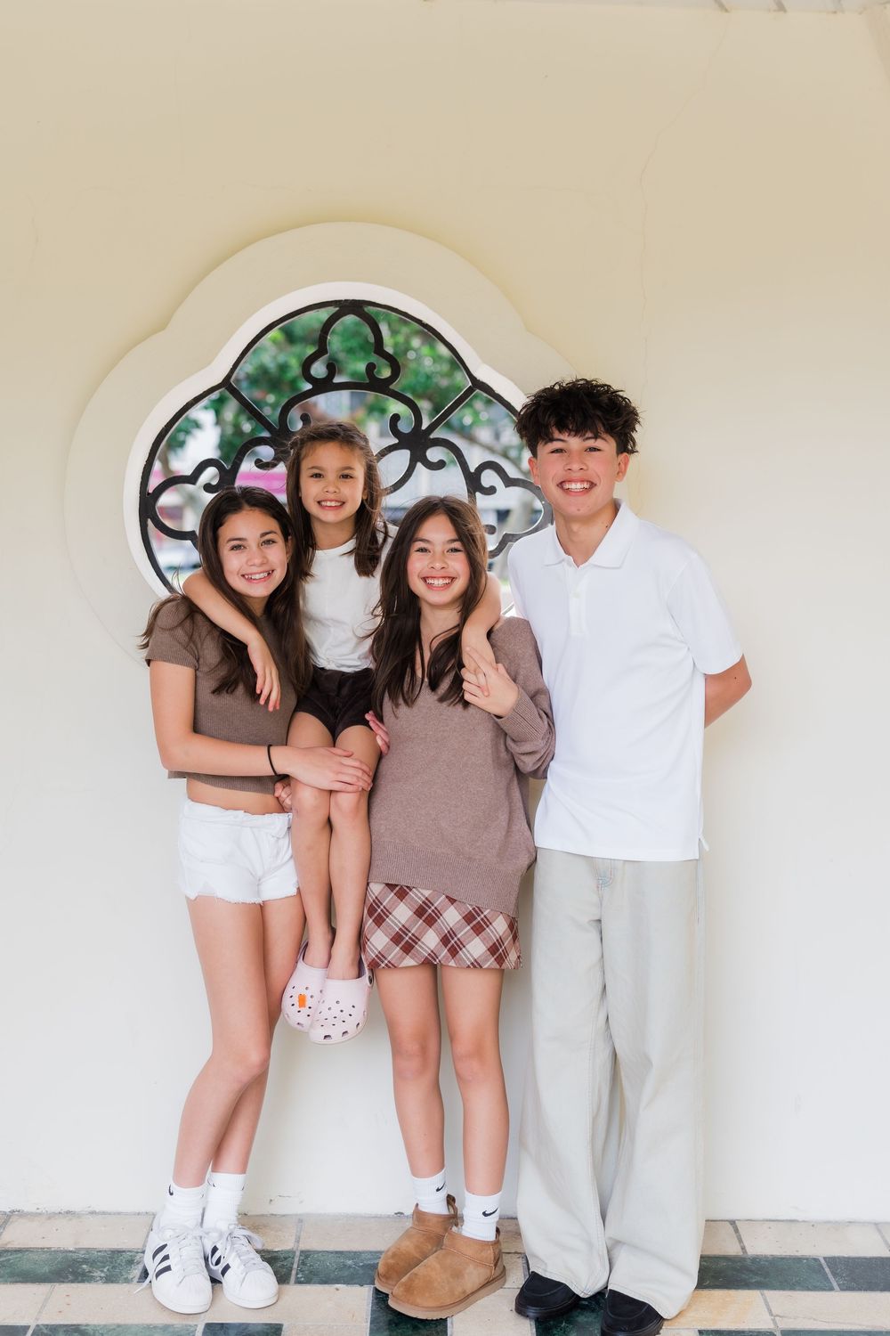 A group poses together in front of a decorative arched wall with an ornate green stained glass window design.