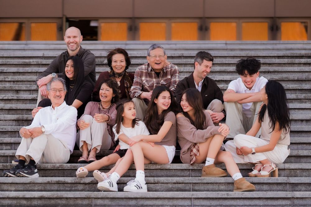 A group of people sitting and laughing together on concrete steps in casual white outfits.
