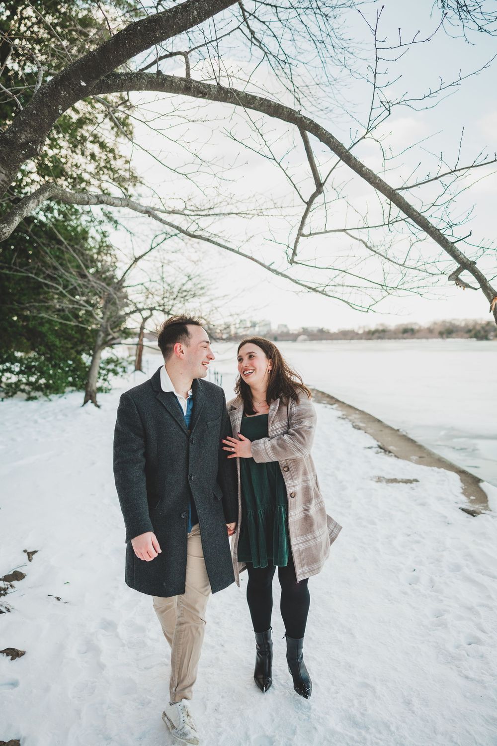 A couple takes a romantic winter walk together along a snowy path through bare trees on a bright afternoon.
