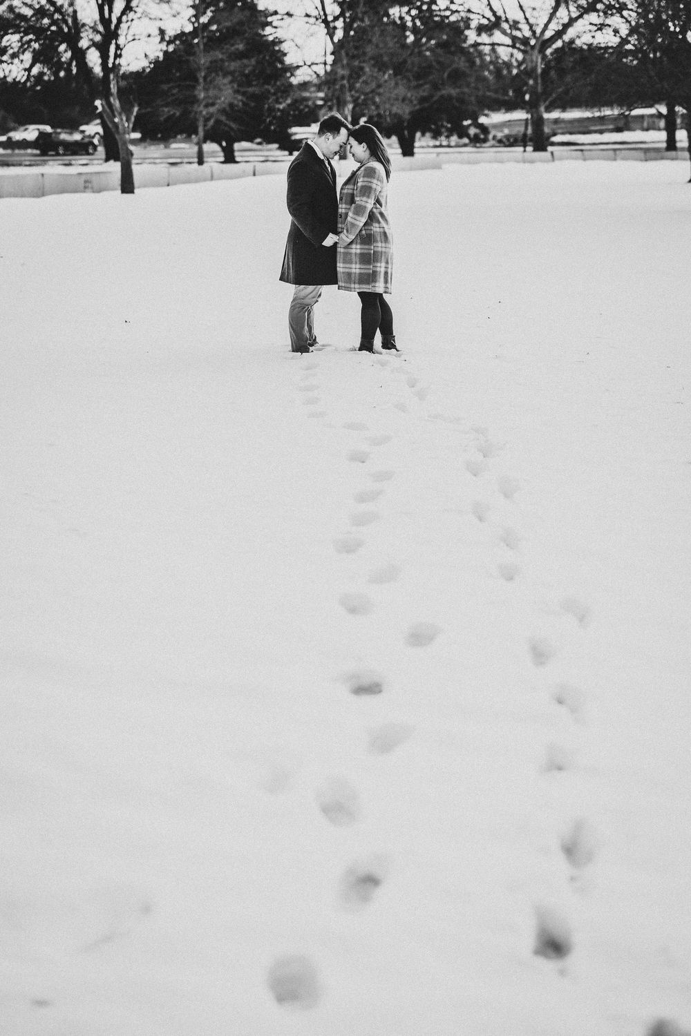 Footprints trail through fresh snow in a winter park landscape.