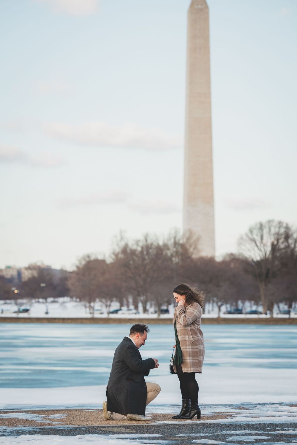A guy proposing in front of the Washington Monument on a winter day with the Tidal Basin and bare trees in the background.