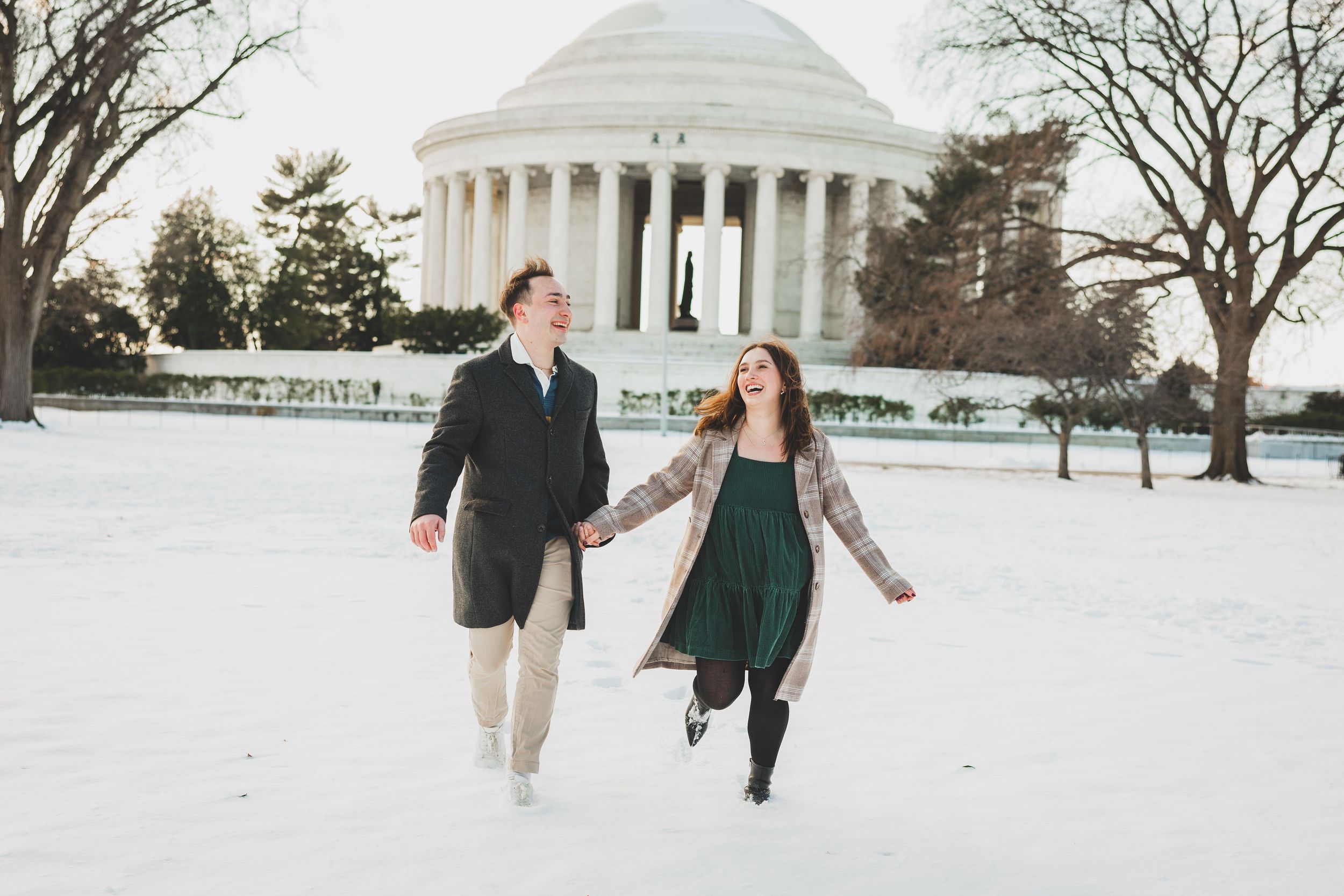 A couple walks together in winter near the Jefferson Memorial with snow-covered grounds and bare trees in Washington DC