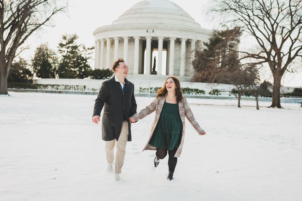 A couple walks together in winter near the Jefferson Memorial with snow-covered grounds and bare trees in Washington DC