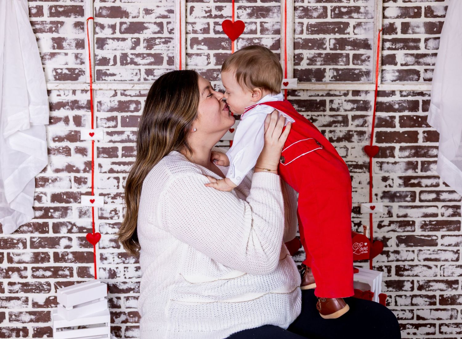 A festive holiday portrait with a white sweater and red accents against a rustic brick wall background.