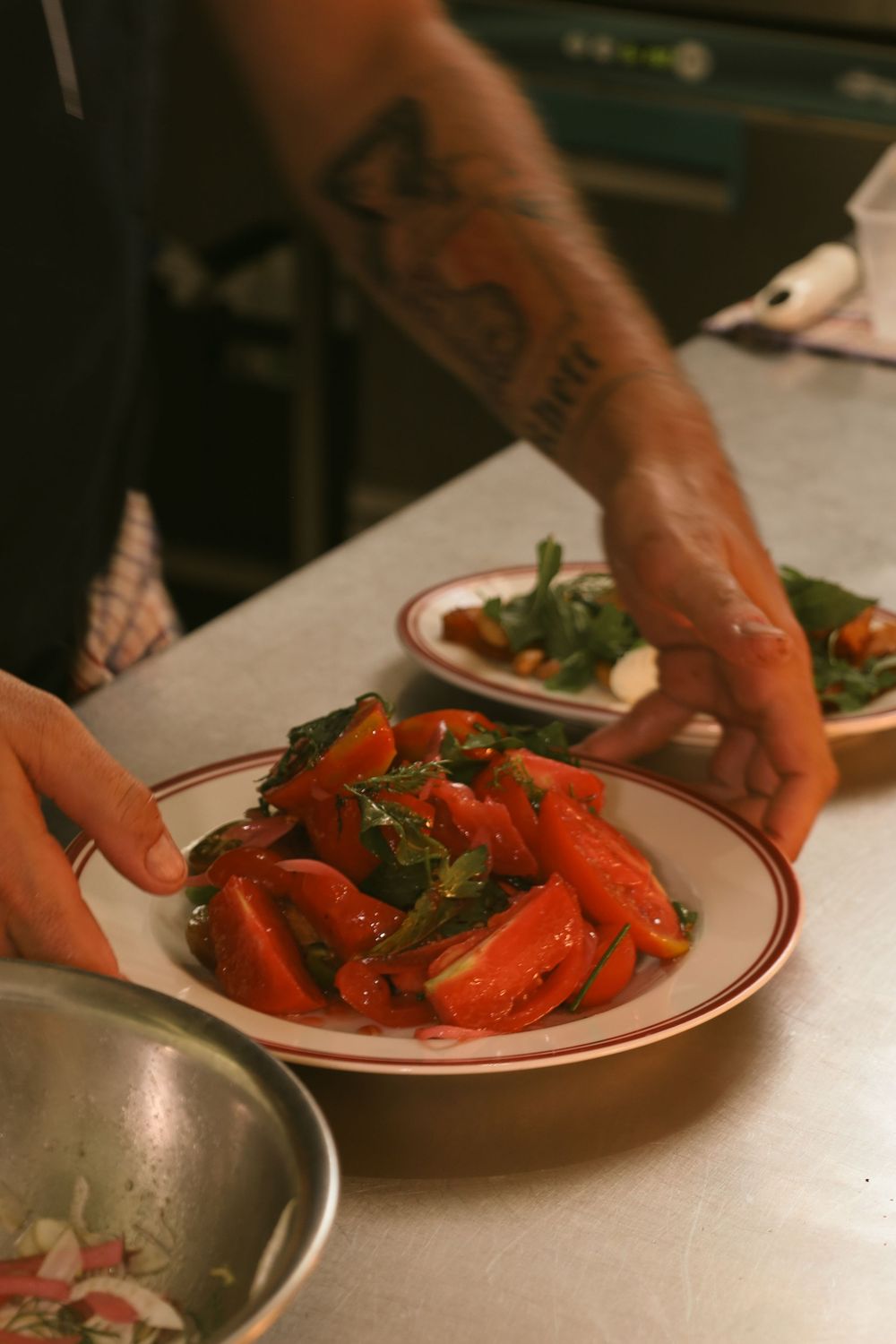 A series of hands placing bright red cooked lobster pieces onto white plates with red trim at a restaurant counter.