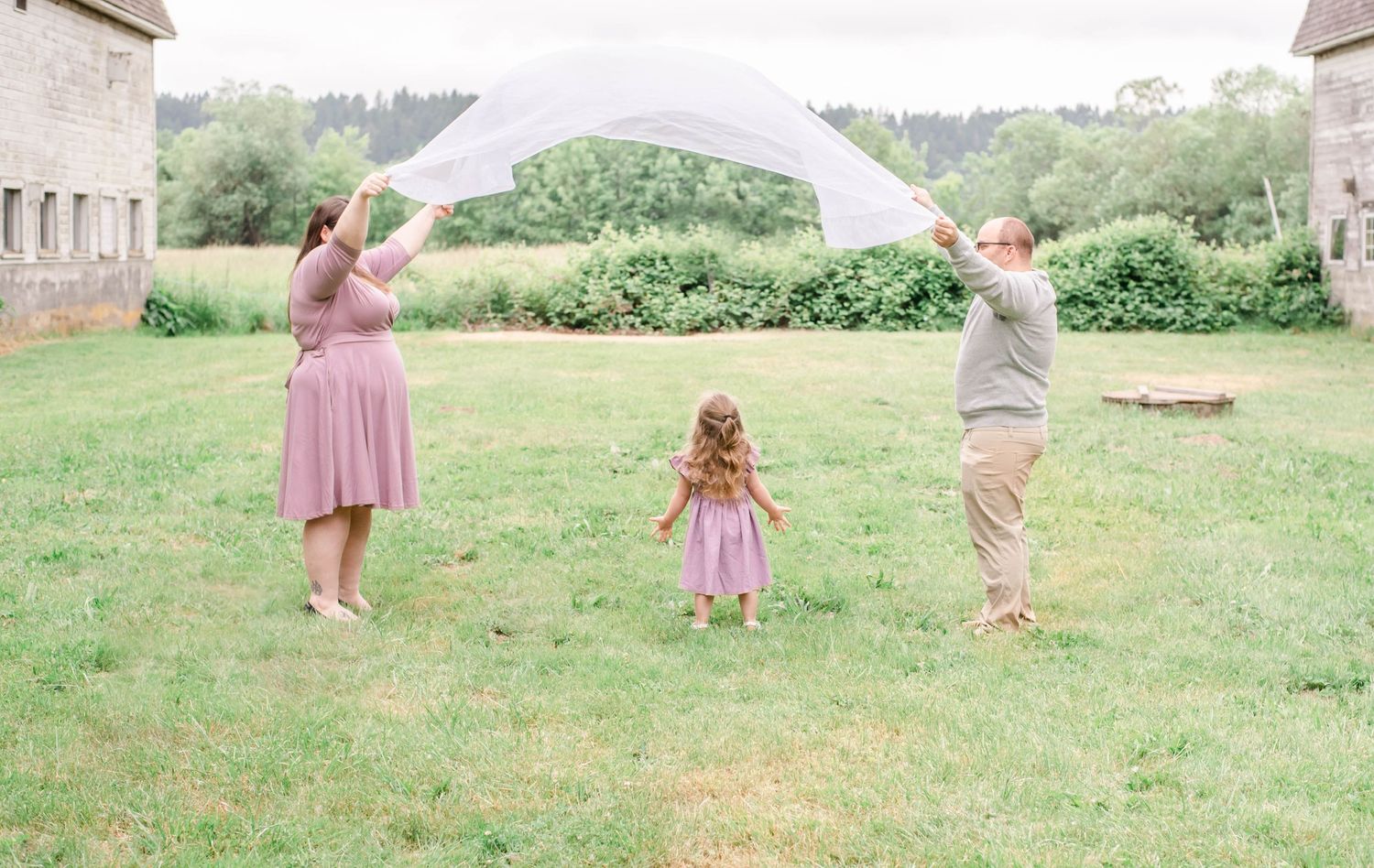 A family shares joyful moments together in a sunlit meadow with mountains visible in the background.