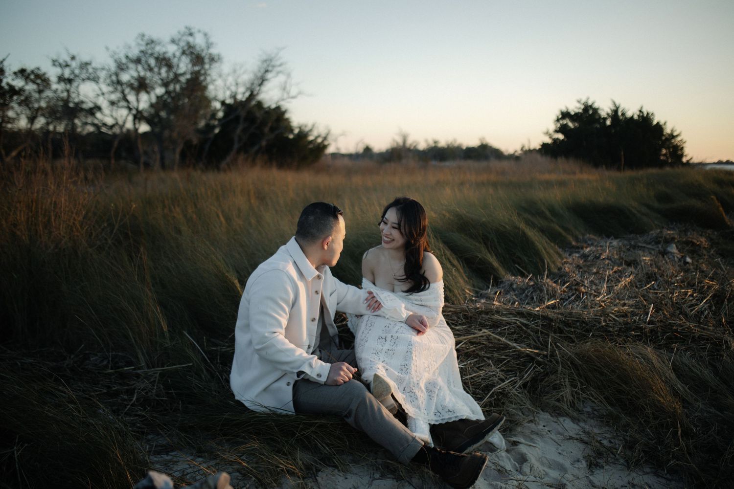 Two people in white coats sit outdoors examining papers and documents at sunset.