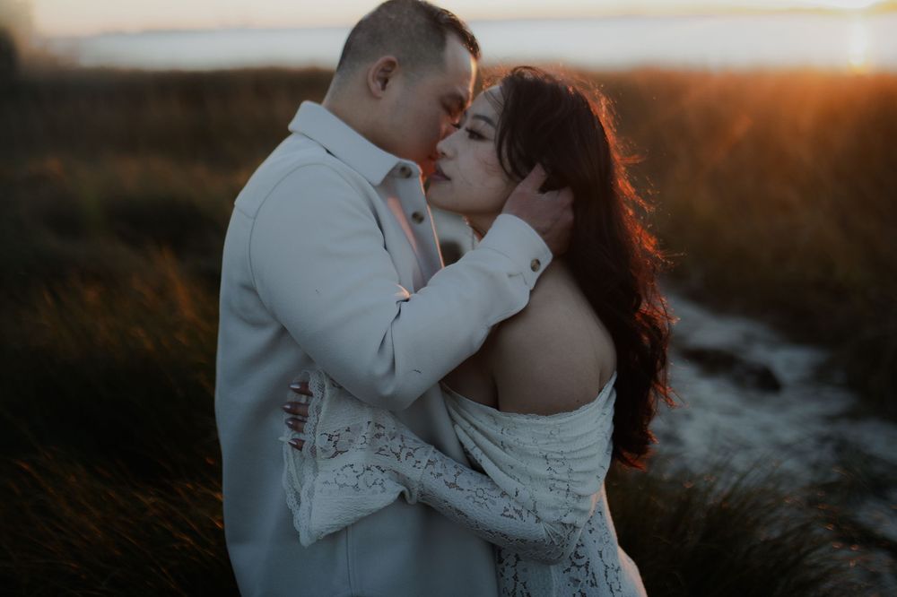 A romantic couple embraces during golden hour sunset by the ocean, creating a dreamy silhouette against the warm light.