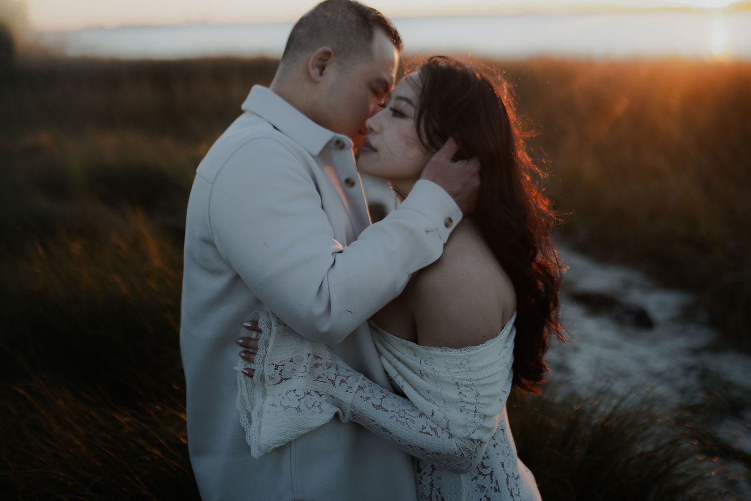 A romantic couple embraces during golden hour sunset by the ocean, creating a dreamy silhouette against the warm light.