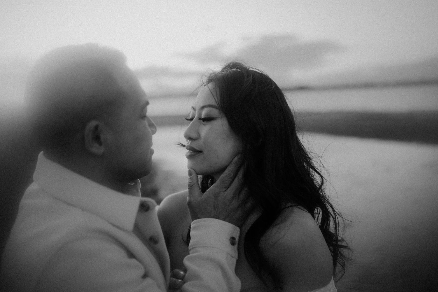 A romantic black and white photo series showing a couple embracing on a beach at sunset.