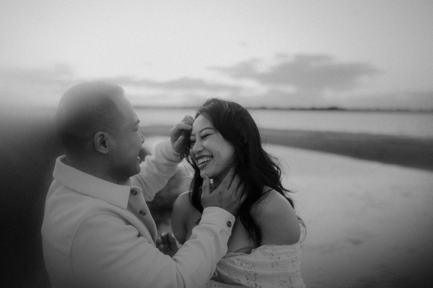 A romantic couple shares intimate moments on a beach in black and white photography.