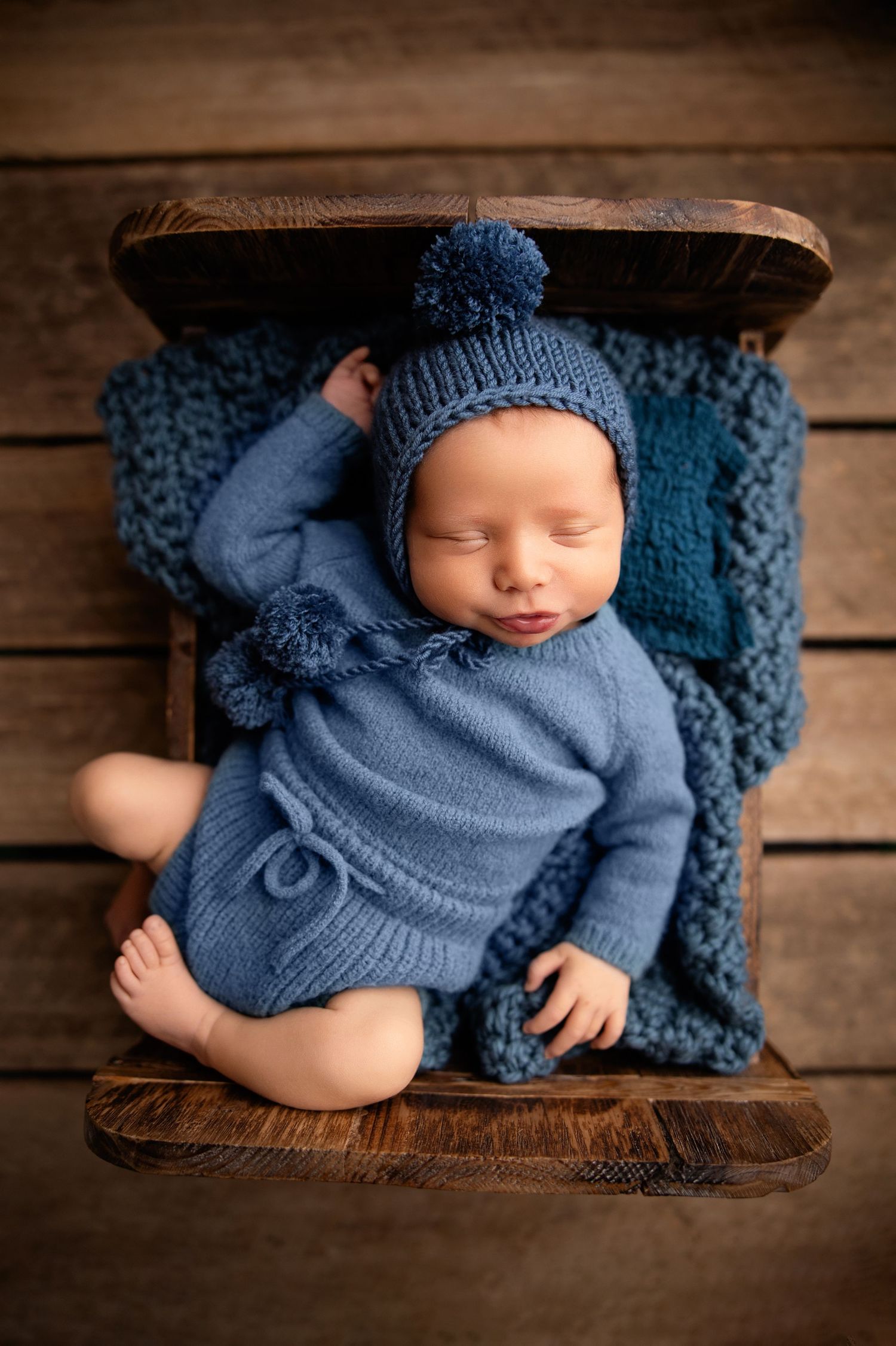 Sleeping newborn baby boy posed in a wooden bed wearing a bonnet during a Middle Tennessee newborn photography session