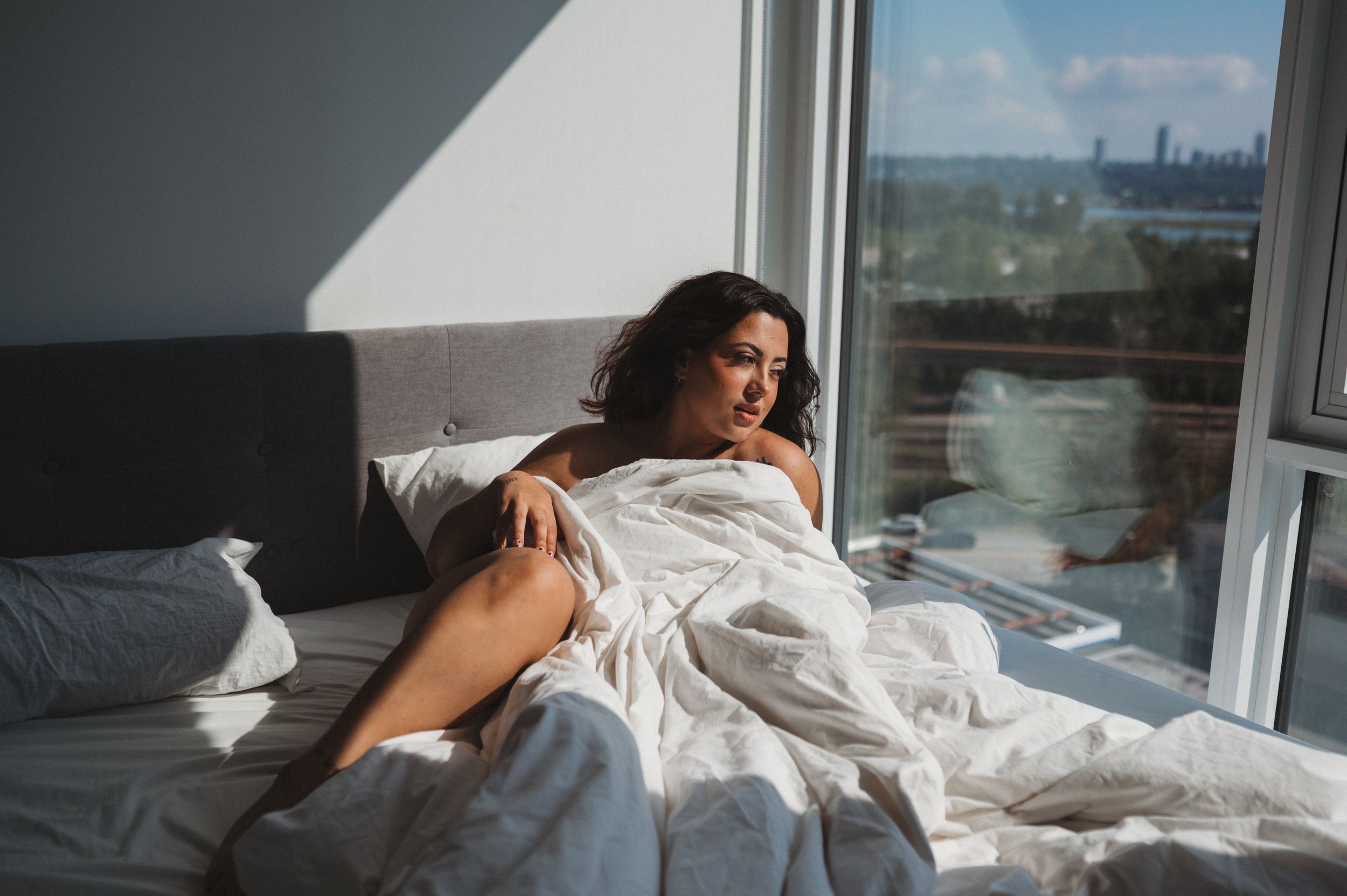 Sunlit bedroom scene with a person relaxing on white bedding near a window.