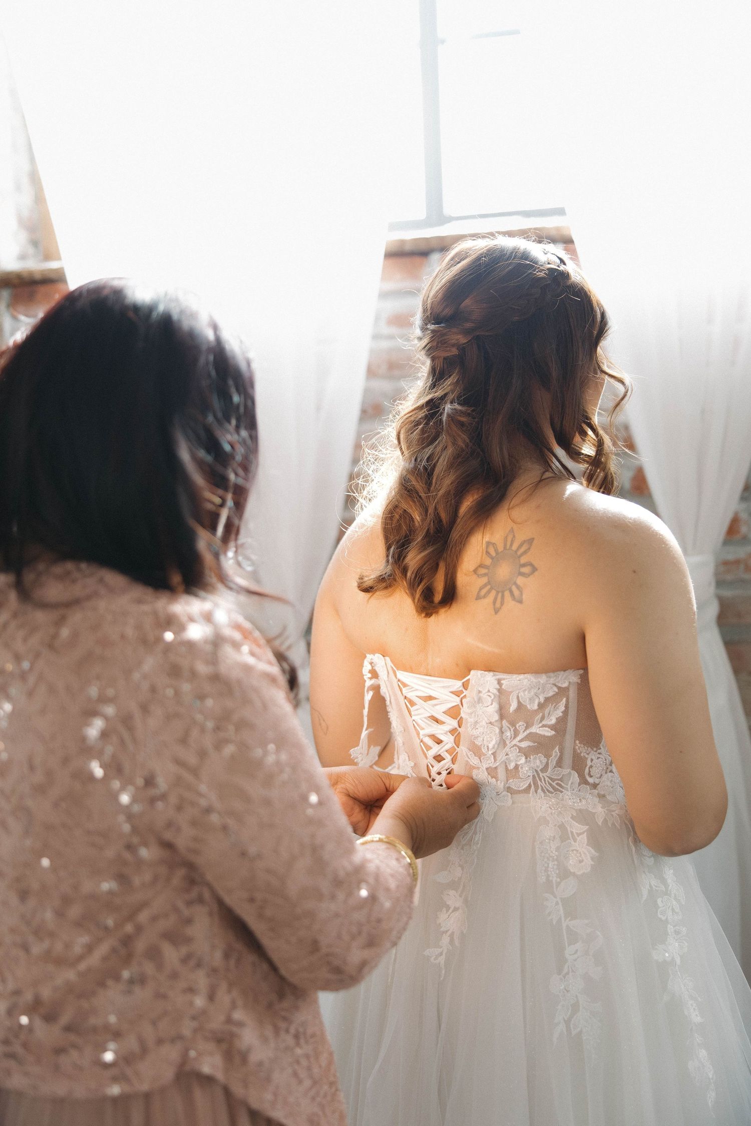 A wedding dress being laced up from behind, showing intricate lace details and a delicate corset back.
