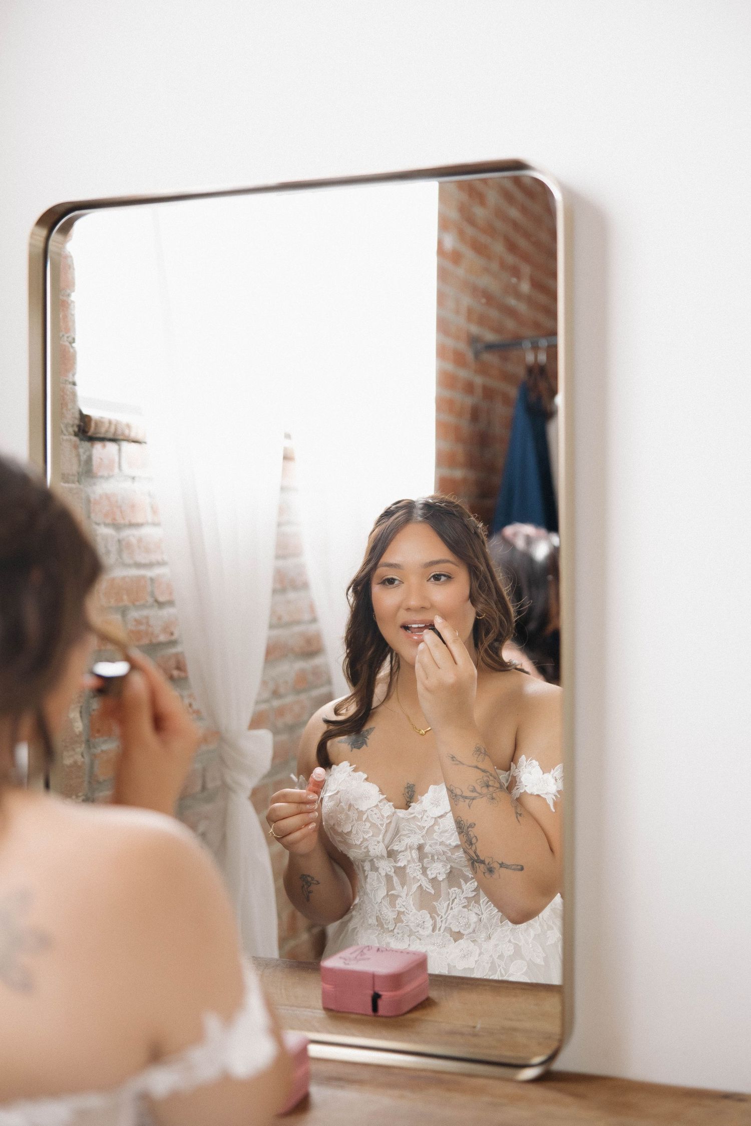 A series of mirror reflections show someone in a white lace wedding dress getting ready and applying makeup.