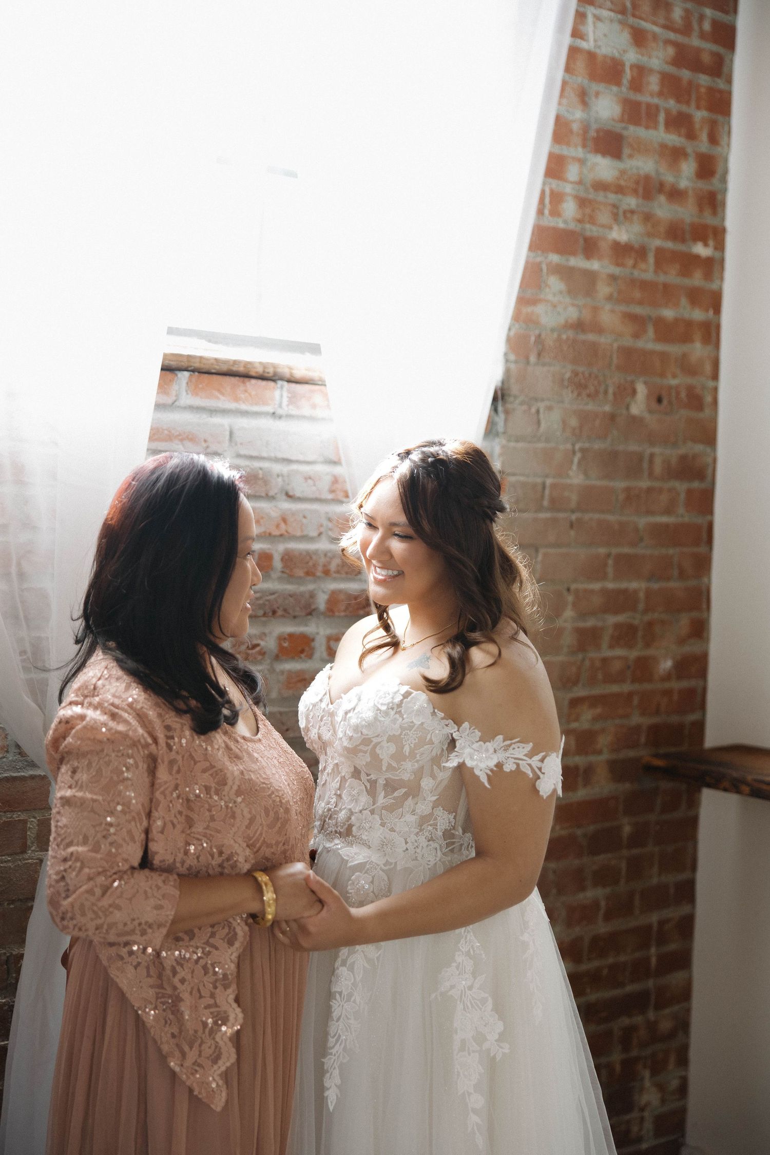 A tender moment during wedding preparations in a rustic brick-walled room.