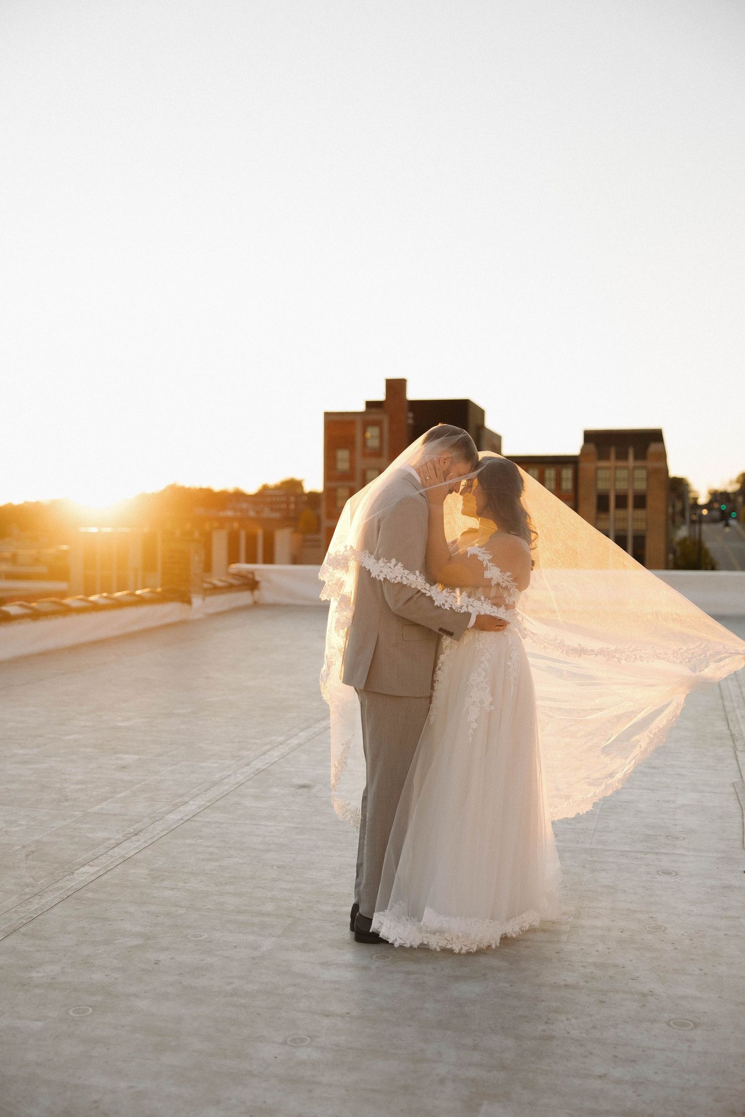 A romantic sunset rooftop wedding moment with a flowing veil catching the golden light.