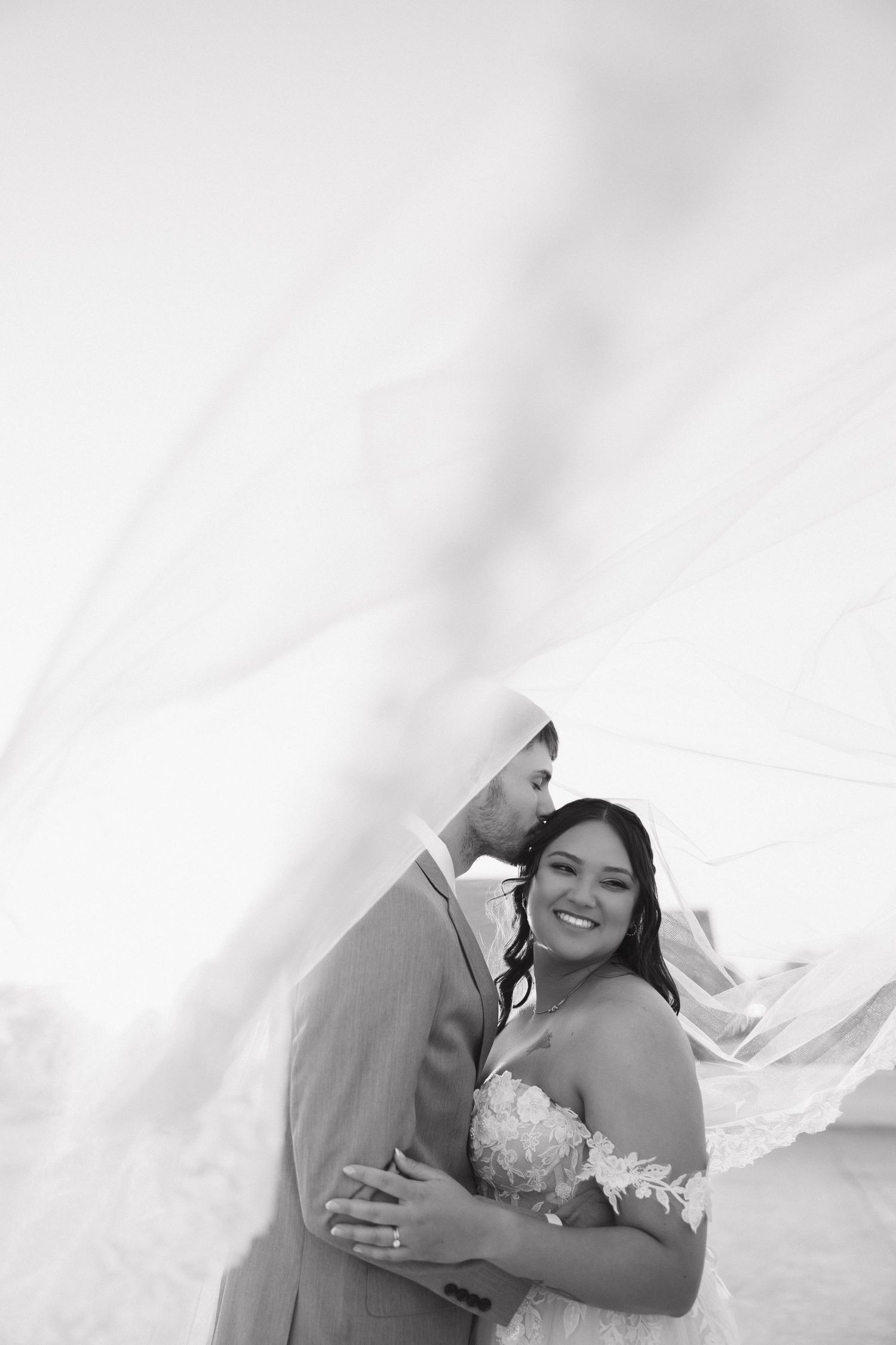 A romantic black and white wedding portrait with flowing veil and elegant attire.