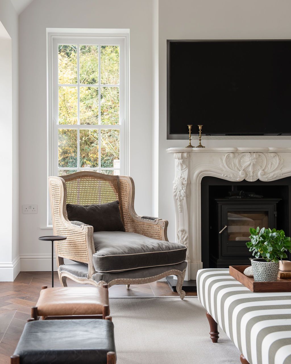 A bright living room with striped armchairs, a vintage chaise lounge, and large windows letting in natural light.