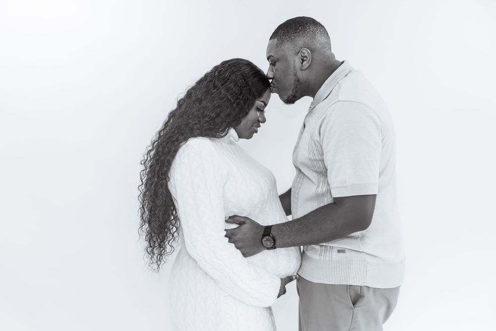 Black and white maternity photo of a couple tenderly touching foreheads while embracing the baby bump.