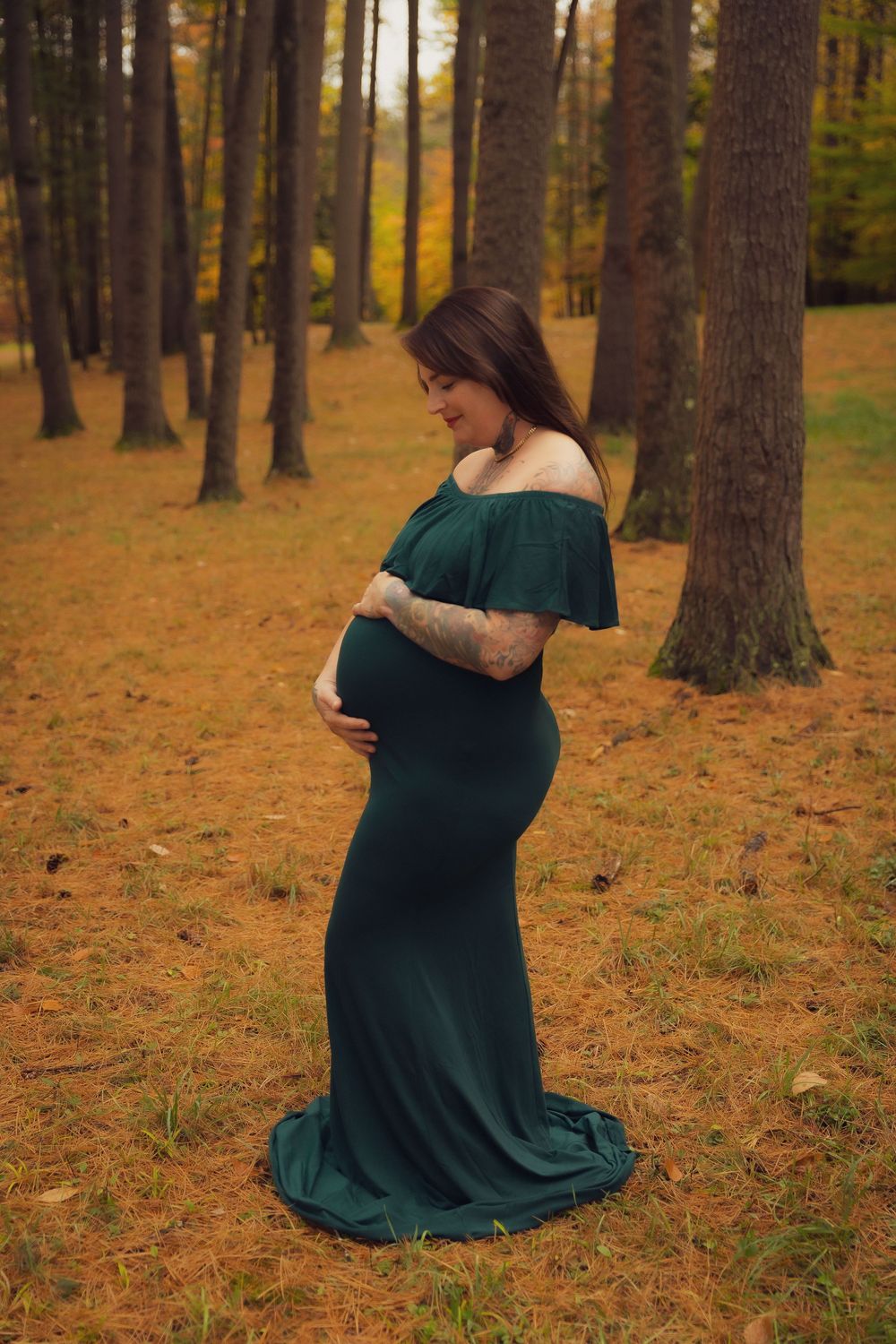 Pregnant woman in green maternity gown lovingly cradles her baby bump in a fall forest.