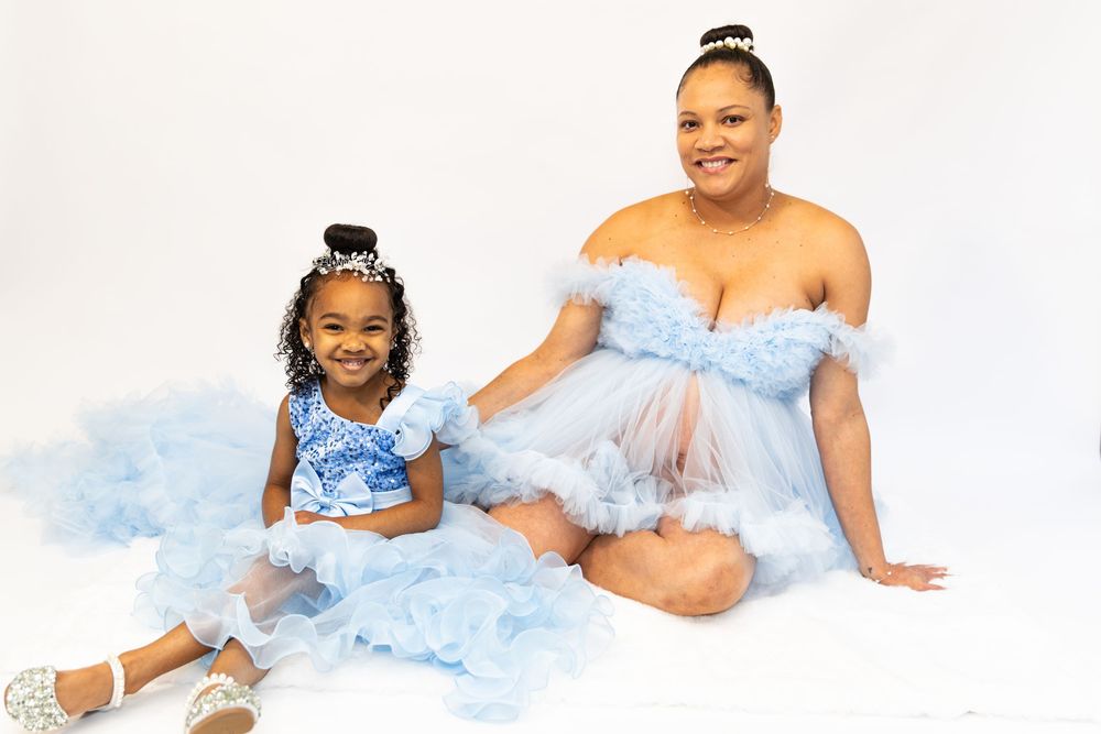 A woman and young girl pose in matching light blue ruffled tulle dresses against a white background for a mother daughter maternity session.