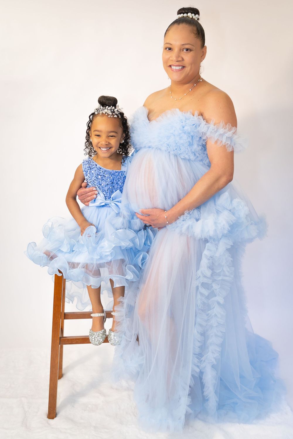 Pregnant woman and young girl in matching blue ruffle gowns pose together in a studio maternity photo shoot.
