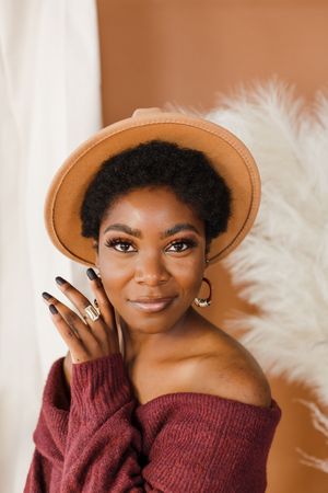 A stylish portrait series showing someone wearing a brown hat and burgundy sweater against a white fluffy backdrop.