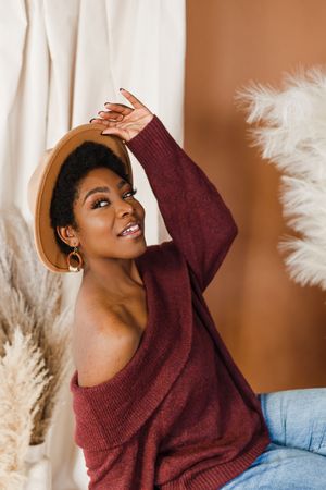 A person in a burgundy sweater poses joyfully against a brown background with white pampas grass decor.