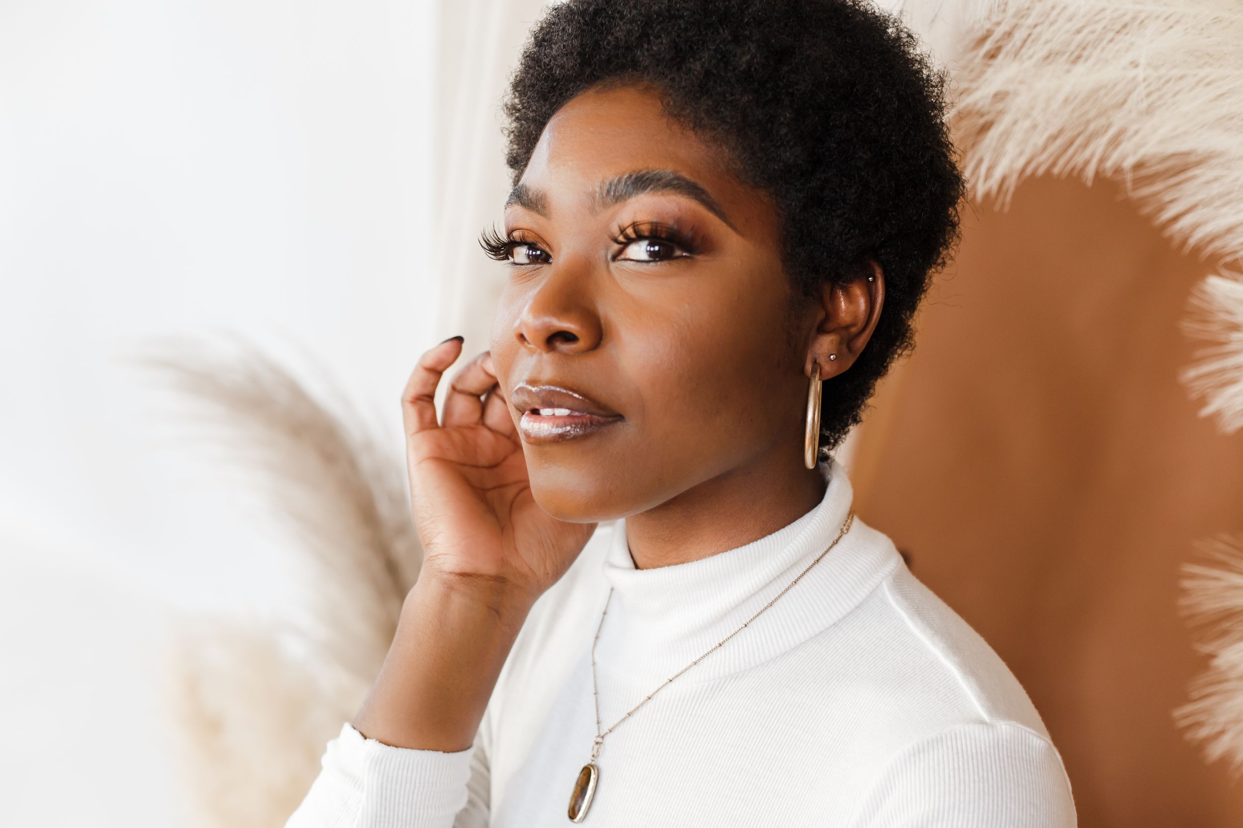 Professional beauty portrait with warm lighting against a neutral background showcasing natural makeup and glowing skin.