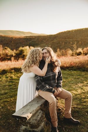 Couple sharing a romantic moment at golden hour on a rustic log bench with autumn hills in the background.