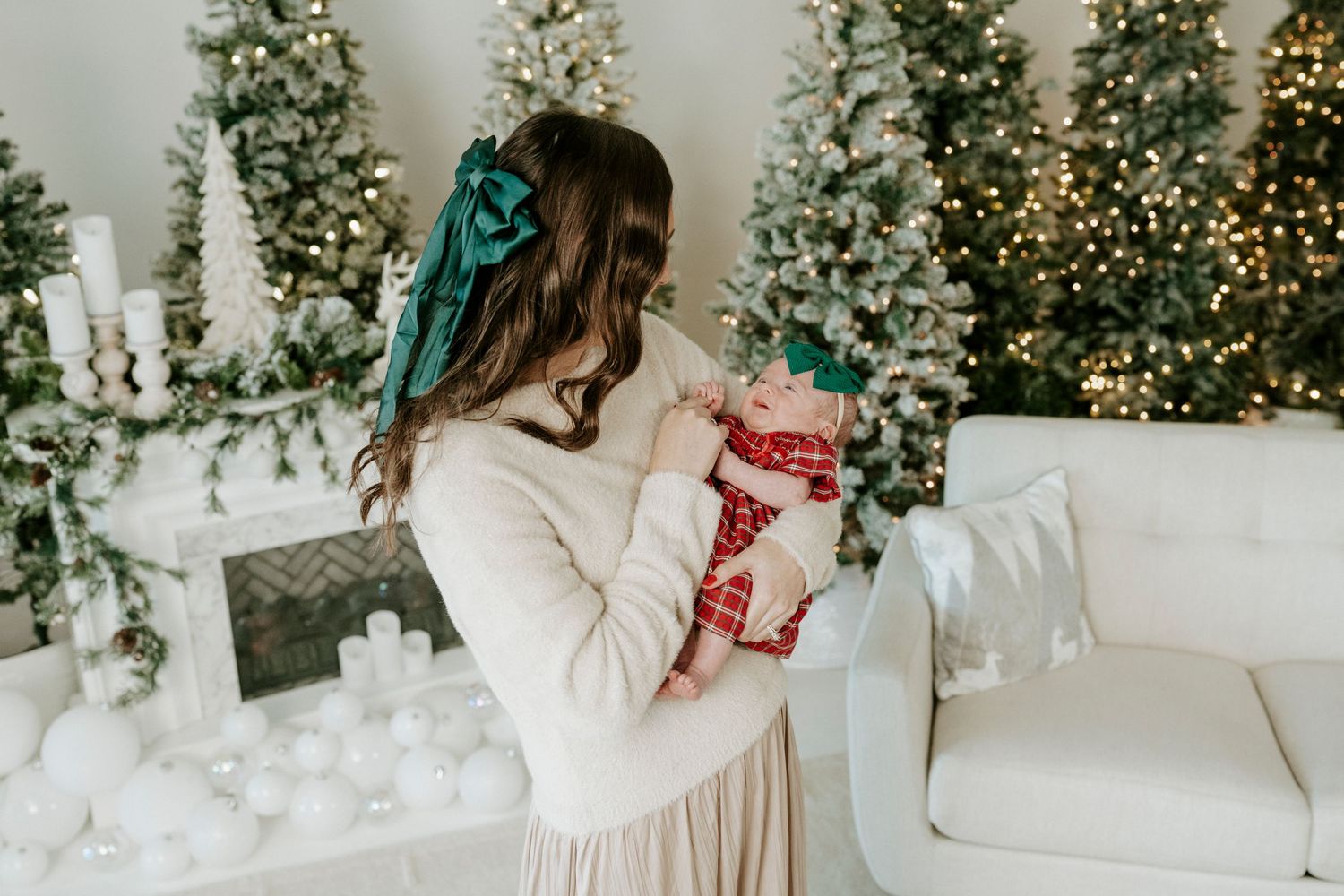 A cozy winter scene with a white couch, flocked Christmas trees, and twinkling holiday lights in the background.