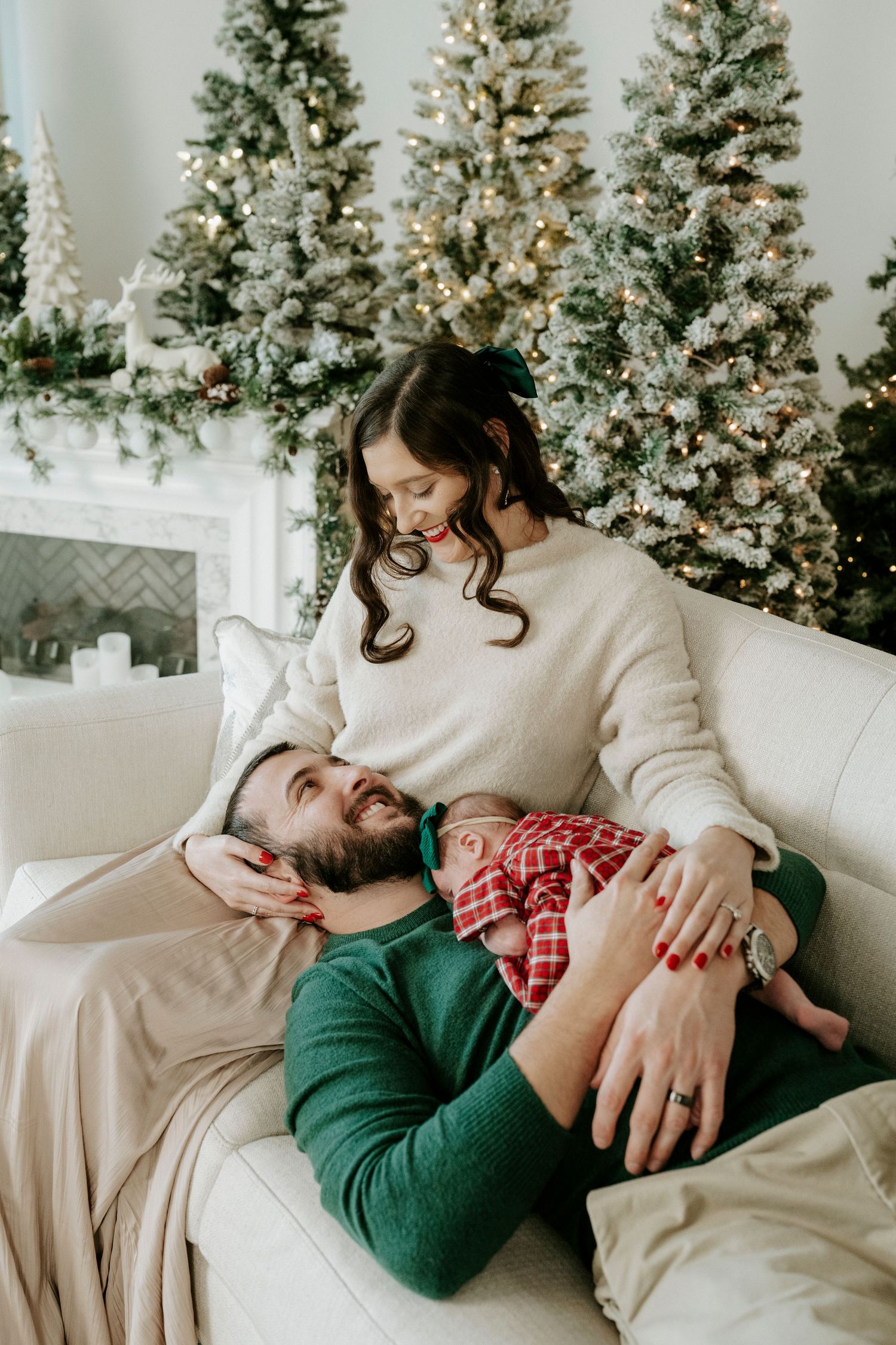Couple shares tender moment on white couch with decorated Christmas trees in background.