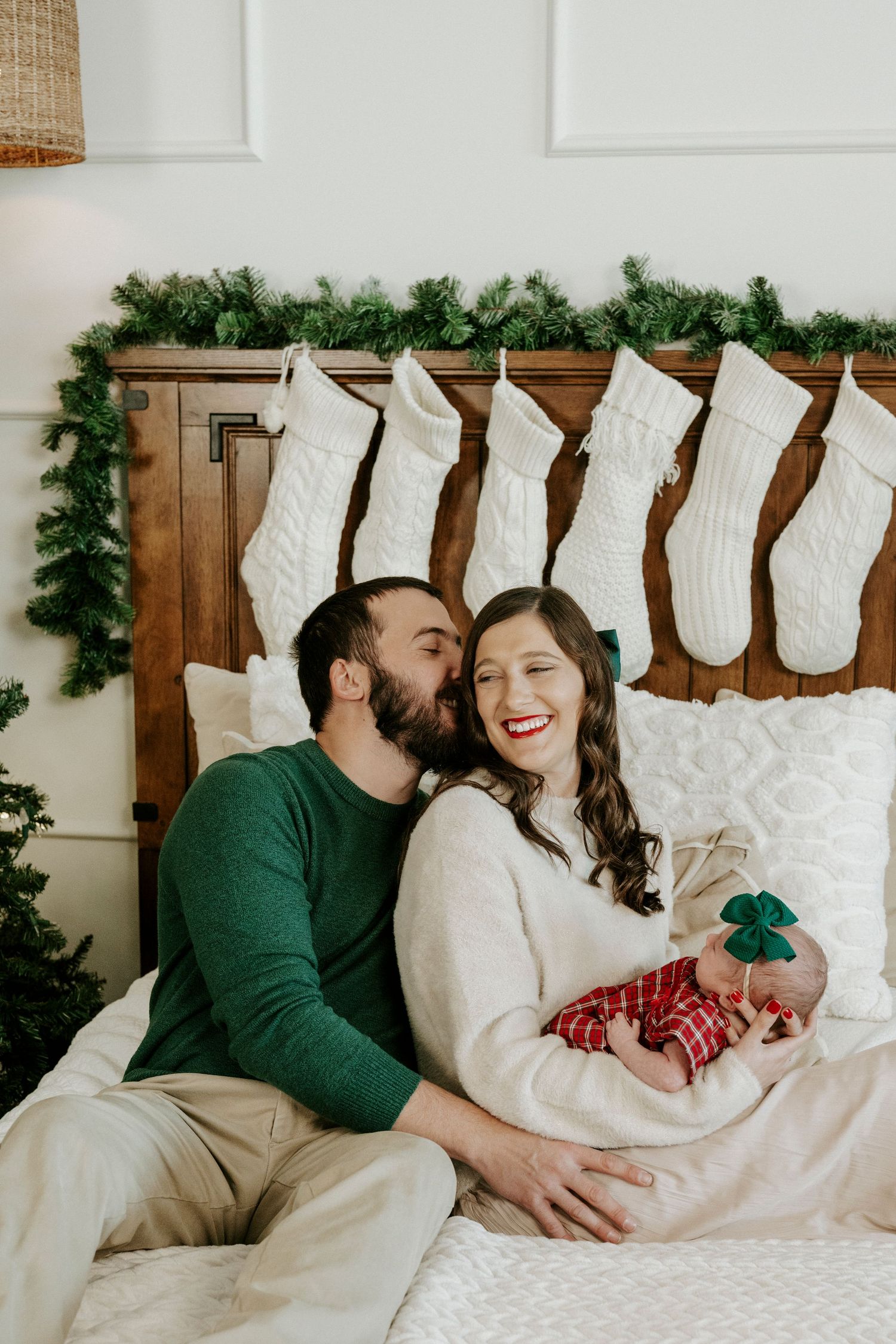 A couple shares tender moments while relaxing on a white bed with Christmas stockings hanging on the wall behind them.