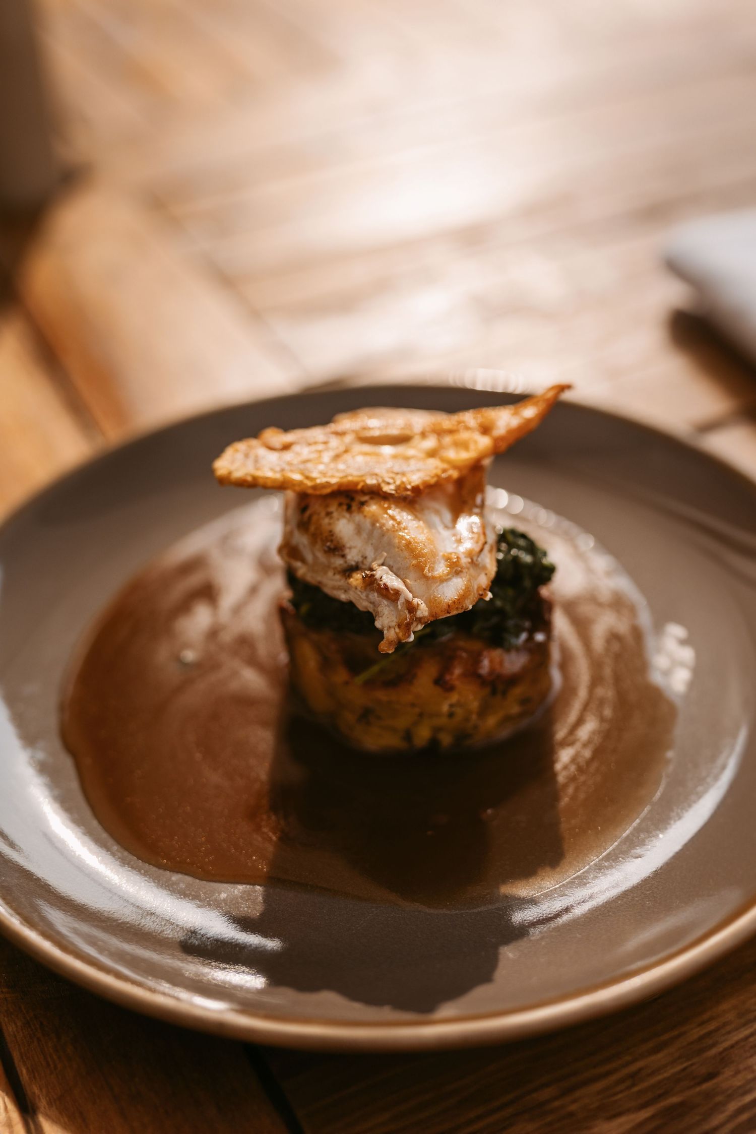 A chocolate brownie with a crackly top crust sits on a brown ceramic plate, photographed in warm lighting.