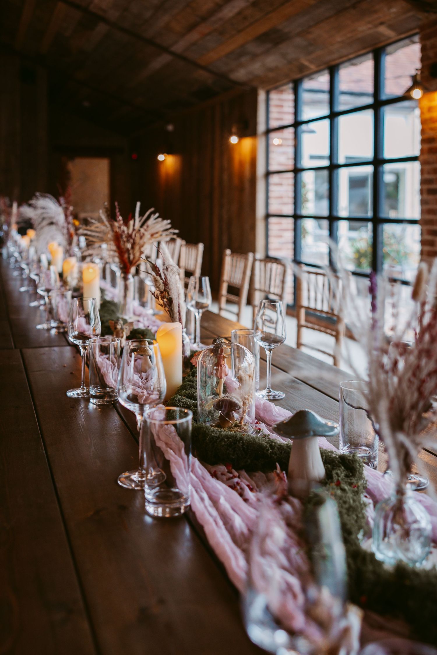 Stratton Court Elegant table setting with glowing candles and pink floral arrangements in a rustic venue with large windows.
