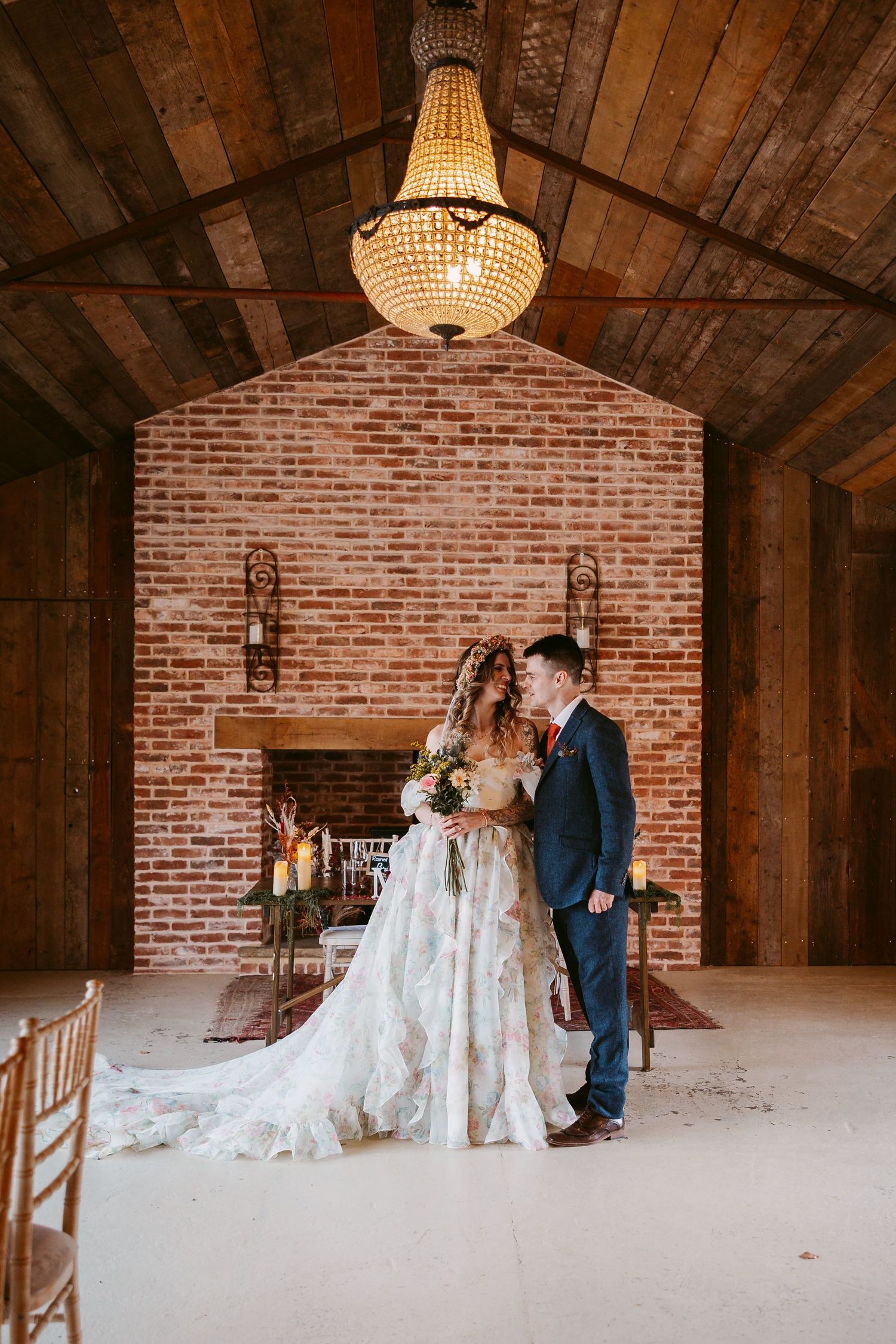 Stratton Court A romantic wedding couple poses in a rustic brick barn venue with elegant chandelier lighting and wooden beams overhead.