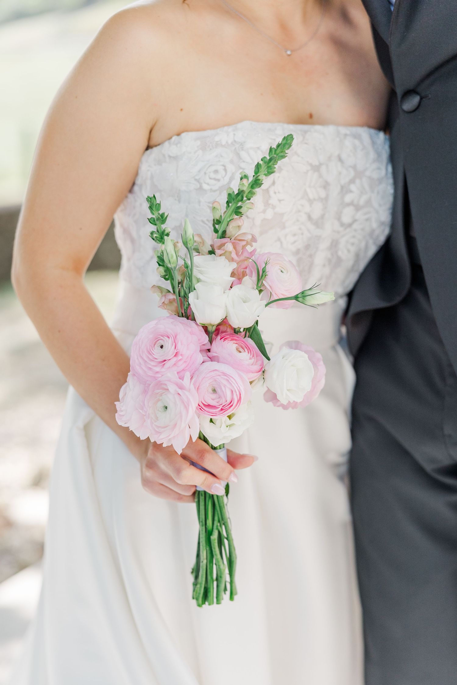 Close-up view of a pink rose and ranunculus bridal bouquet against a white wedding dress.