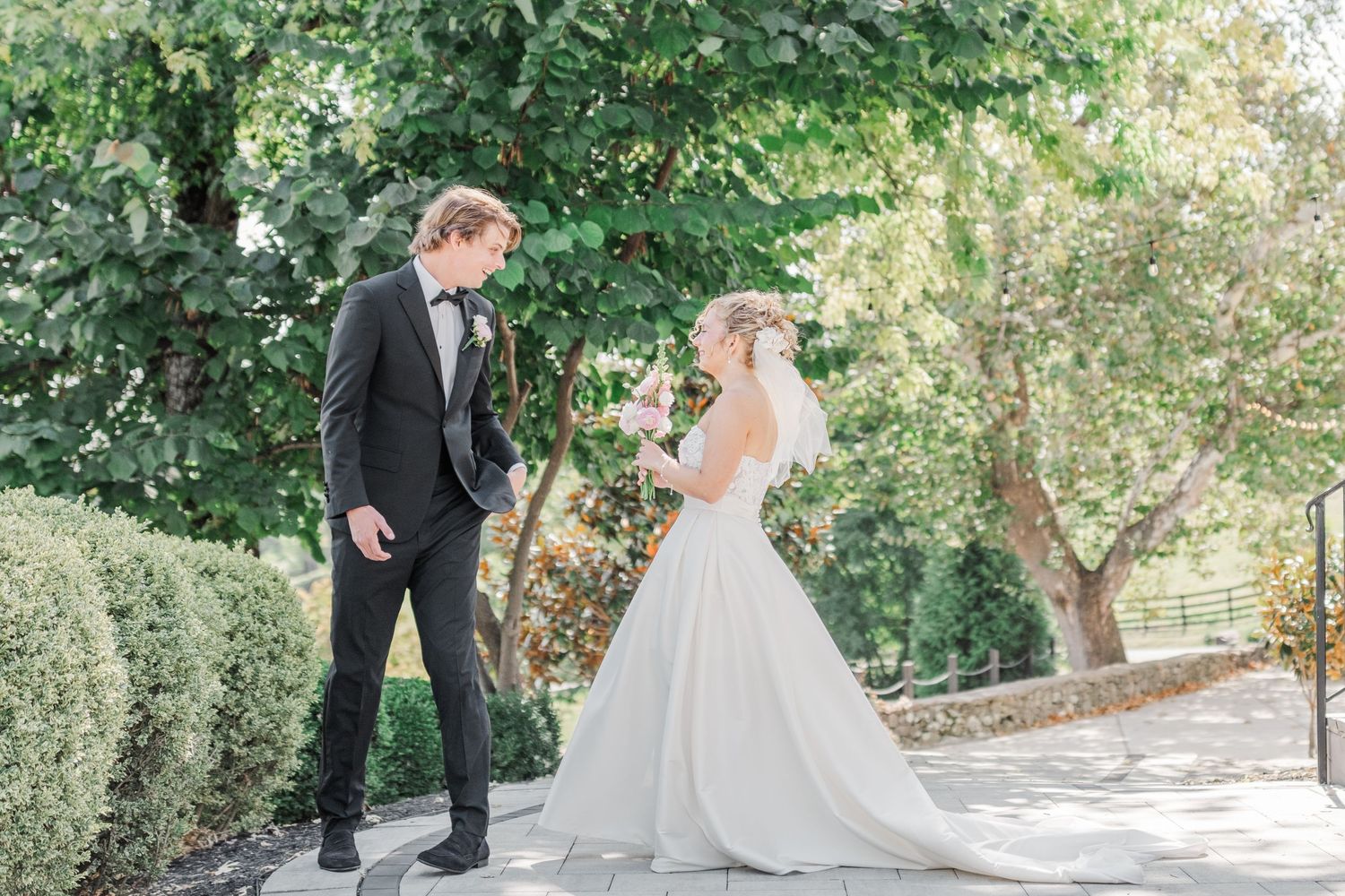Elegant wedding couple poses on stone pathway surrounded by lush green garden scenery.