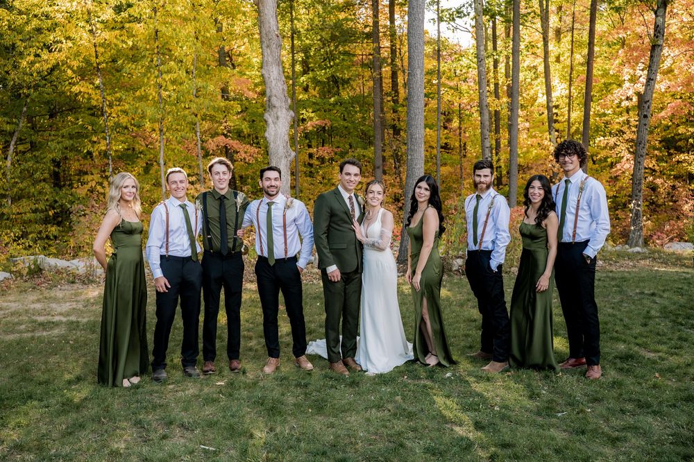 Wedding party stands together in a line against vibrant autumn foliage in an outdoor setting.