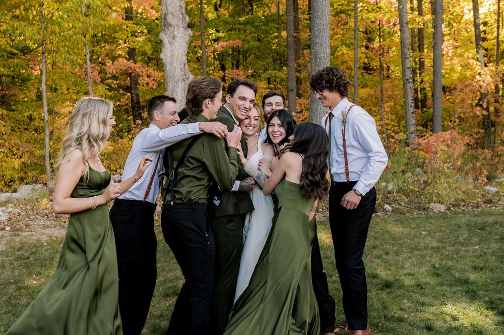 Wedding party shares candid moments in a sun-dappled autumn forest setting with golden leaves and natural light.