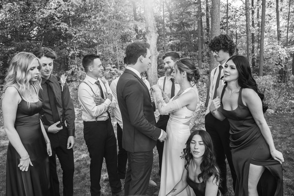 A wedding party celebrates in a wooded outdoor setting with guests mingling and laughing together.
