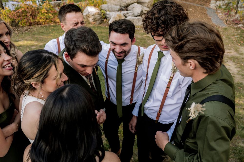 Group laughs together during candid moment at outdoor autumn wedding celebration.