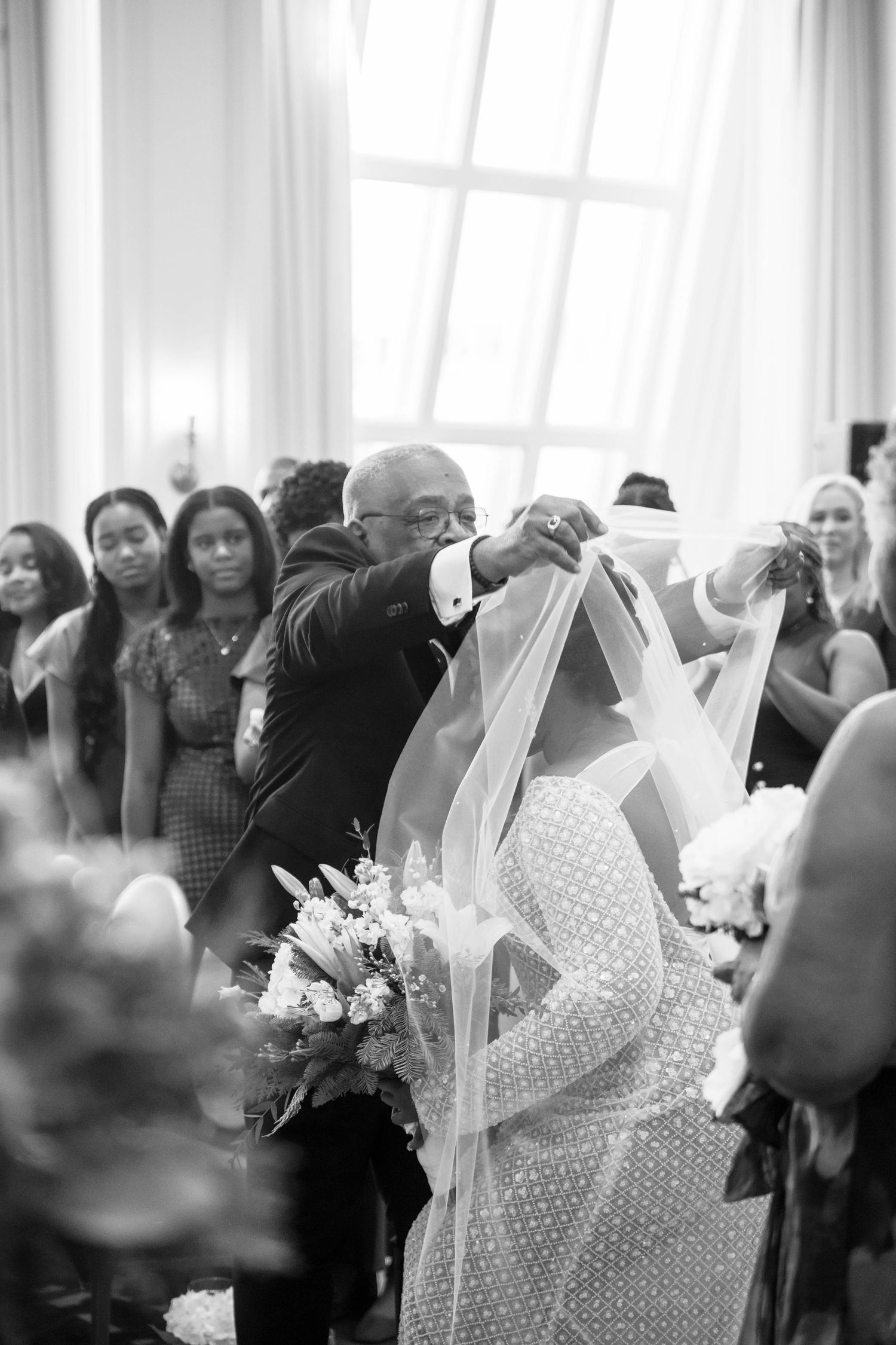 Father of the bride lifting veil during emotional black and white wedding ceremony aisle moment.