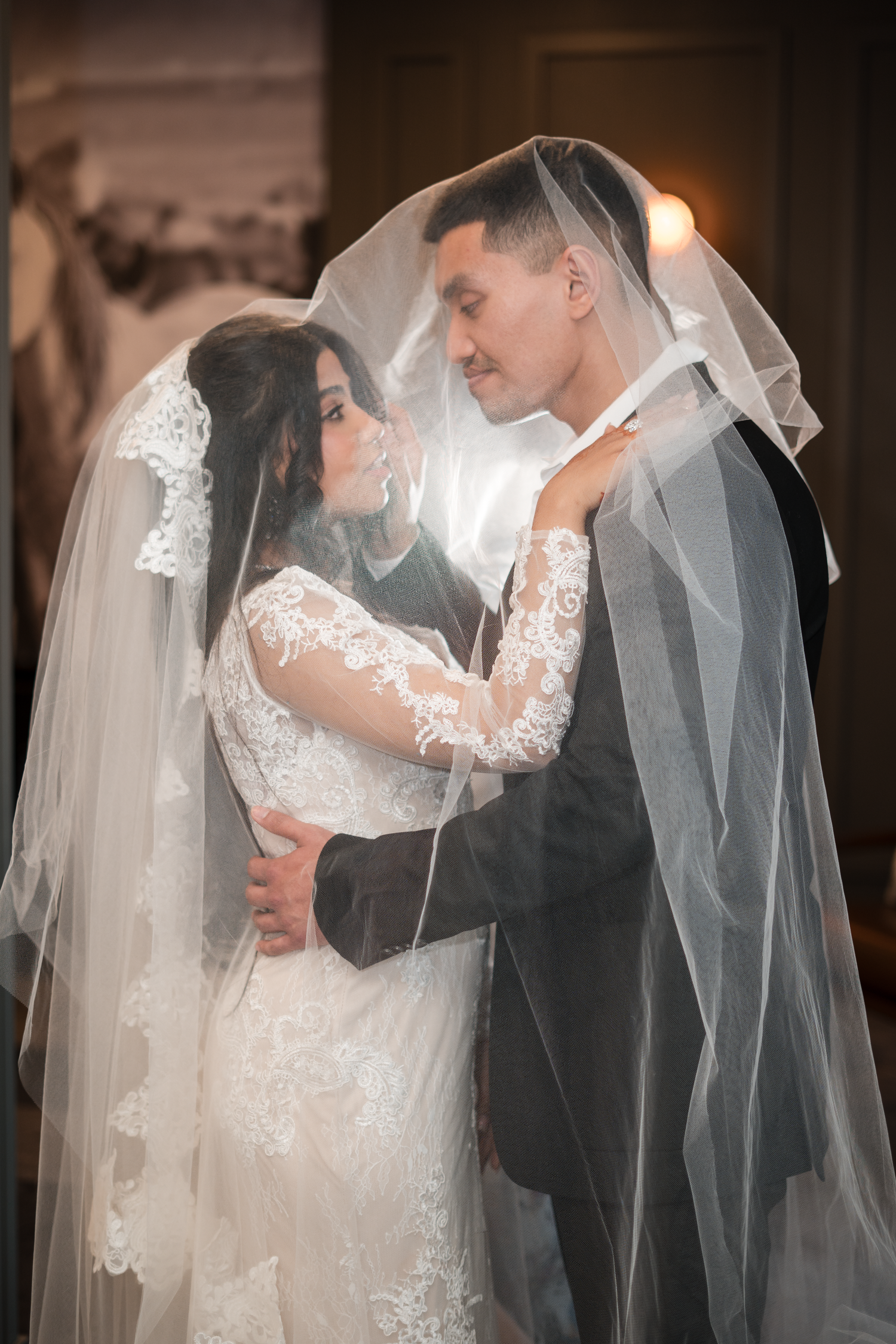 Romantic bride and groom sharing intimate moment together under flowing white lace wedding veil.