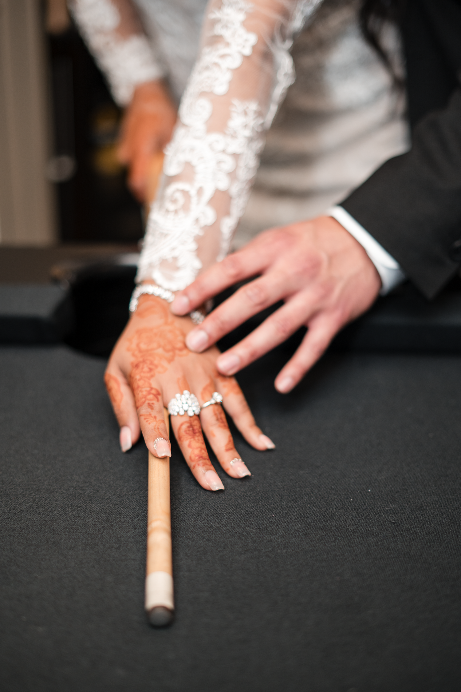 Close-up of bride's henna-decorated hand with diamond rings holding billiard cue on pool table.