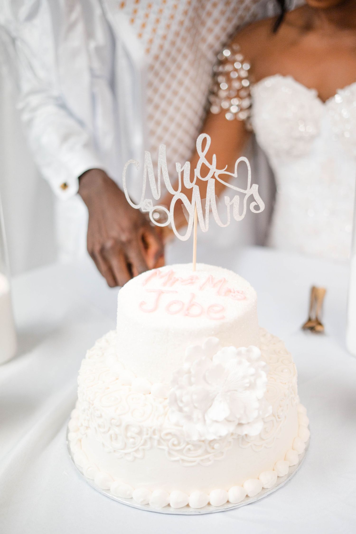 Newlyweds cut elegant white two-tier wedding cake topped with Mr & Mrs cake topper at reception.