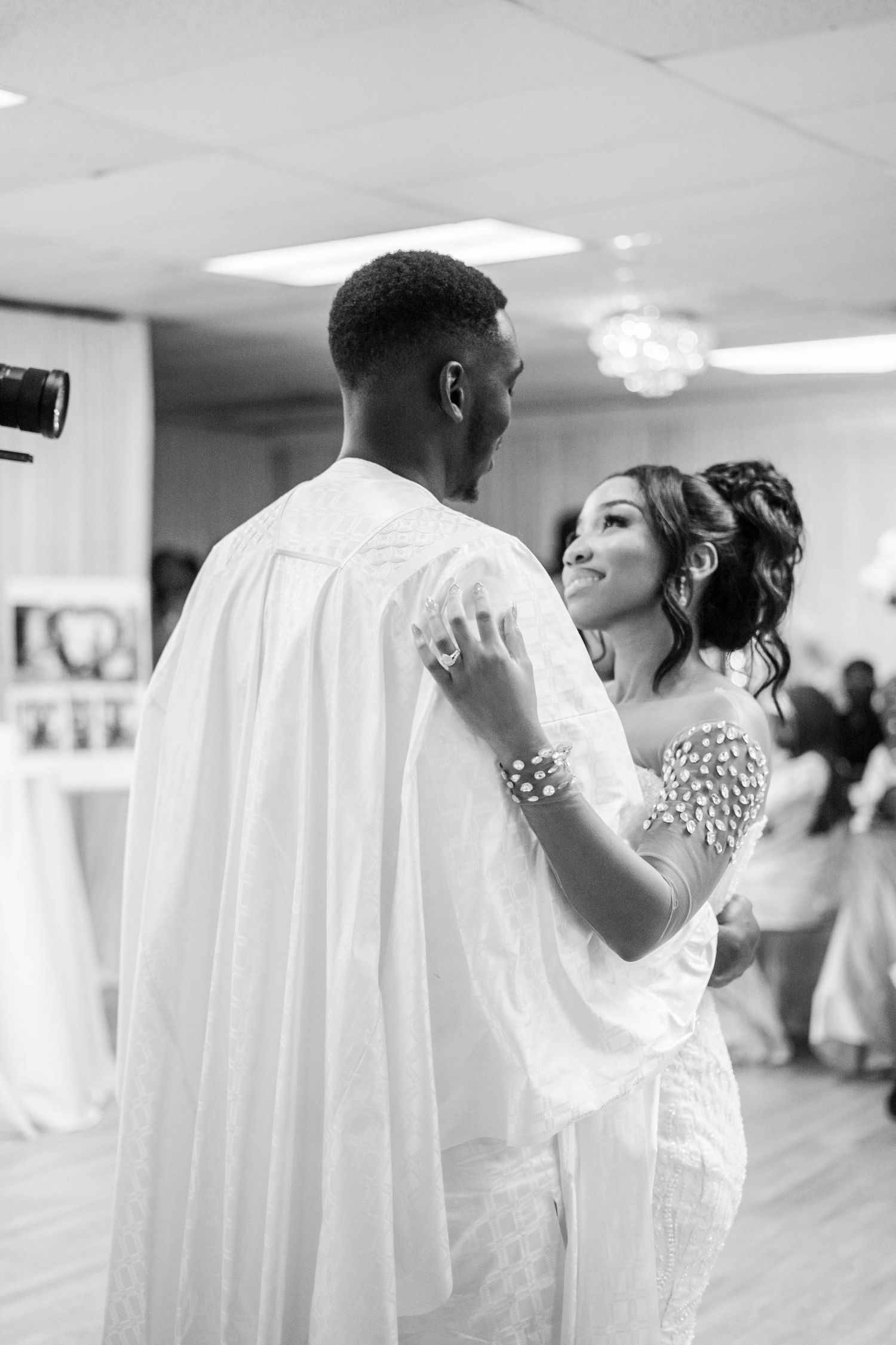 Black and white photo of bride and groom dancing together at wedding reception in elegant venue.